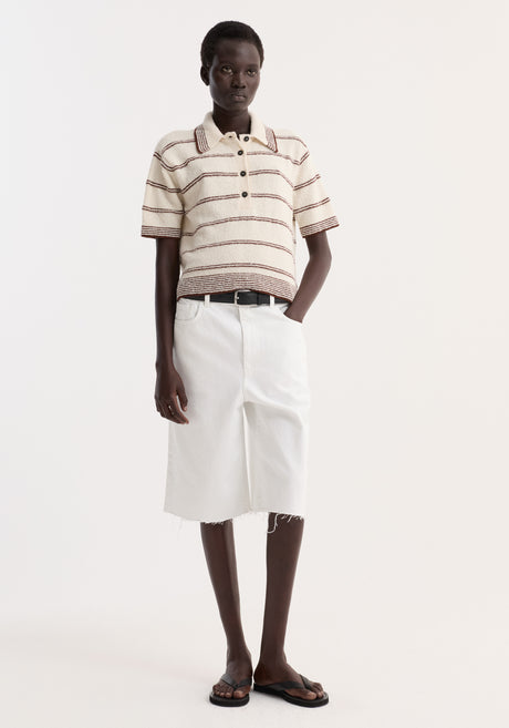 Model showcases Baggy fit denim shorts in optic white, featuring a bermuda length and raw hemline, styled with a cream knit polo and white denim skirt.