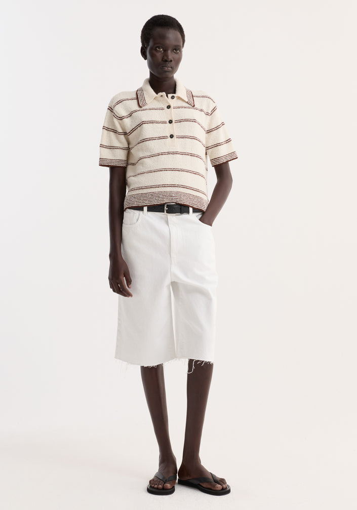 Model showcases Baggy fit denim shorts in optic white, featuring a bermuda length and raw hemline, styled with a cream knit polo and white denim skirt.
