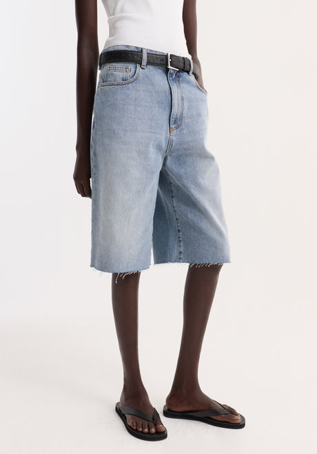 Model wearing Baggy fit denim shorts in classic blue, featuring a relaxed above-the-knee cut with raw hemline, paired with a ribbed tank top and sandals.