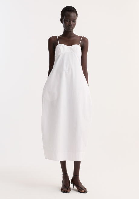 Bustier volume dress in optic white, featuring a sweetheart neckline, adjustable thin straps, and a full skirt, worn by a model in black strappy sandals.