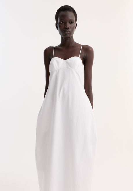 Bustier volume dress in optic white, featuring a sweetheart neckline, adjustable thin straps, and a full skirt, worn by a model in black strappy sandals.