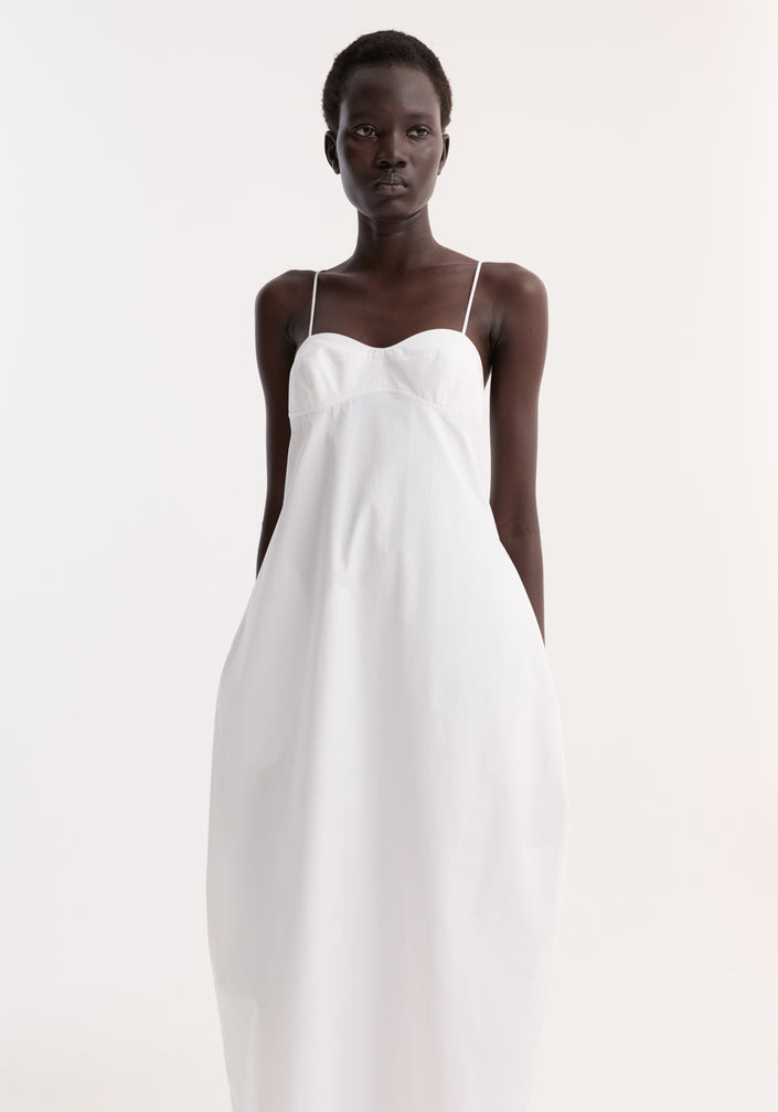 Bustier volume dress in optic white, featuring a sweetheart neckline, adjustable thin straps, and a full skirt, worn by a model in black strappy sandals.