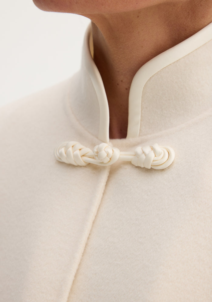 Pankou closure poncho | off white: Close-up of stand collar with intricate pankou closure on a soft wool poncho, highlighting its refined, oversized silhouette.