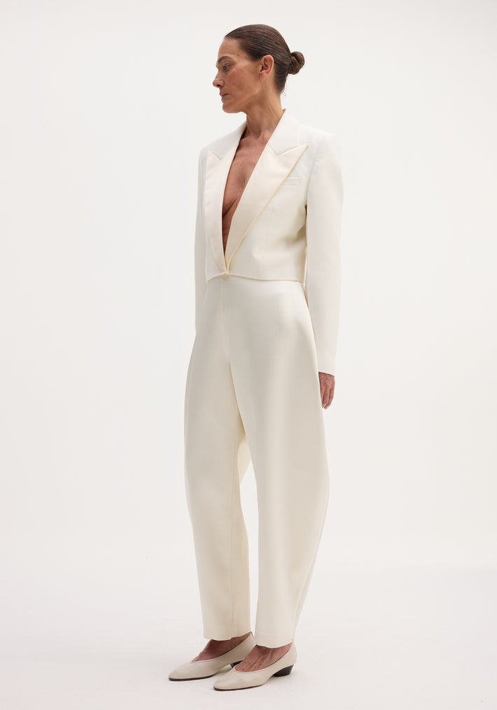 Model in a Cropped blazer | off white with satin peak lapels, high-waisted trousers, and low-heeled shoes, showcasing a sleek, monochromatic look.