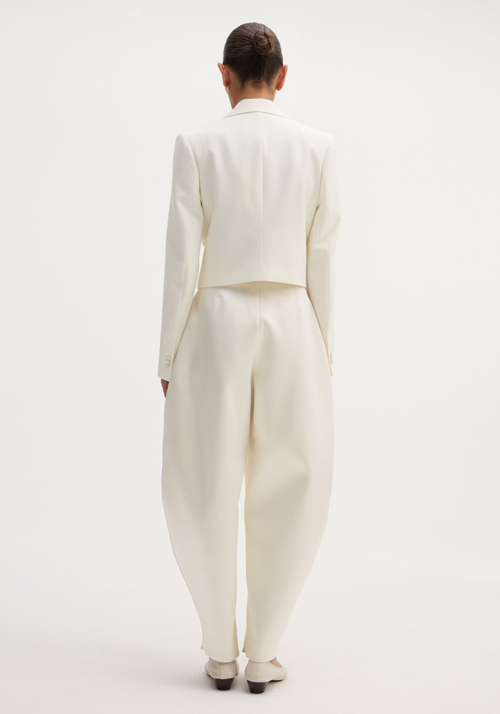 Sculptural satin trousers in ivory with a high waist and balloon leg, paired with a cropped blazer, creating a modern, minimal silhouette.