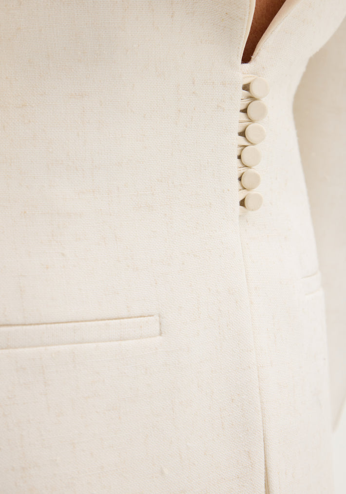 Close-up of the Reversed blazer in winter white, showing the woven texture, fabric-covered buttons, and a welt pocket, highlighting its elegant, structured design.