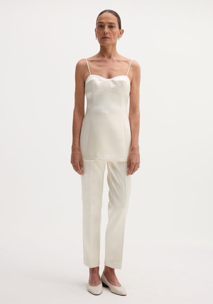 Model wears Satin bustier top | ivory, featuring a fitted bustier-style design, sweetheart neckline, and adjustable back straps, paired with matching trousers and pearl earrings.