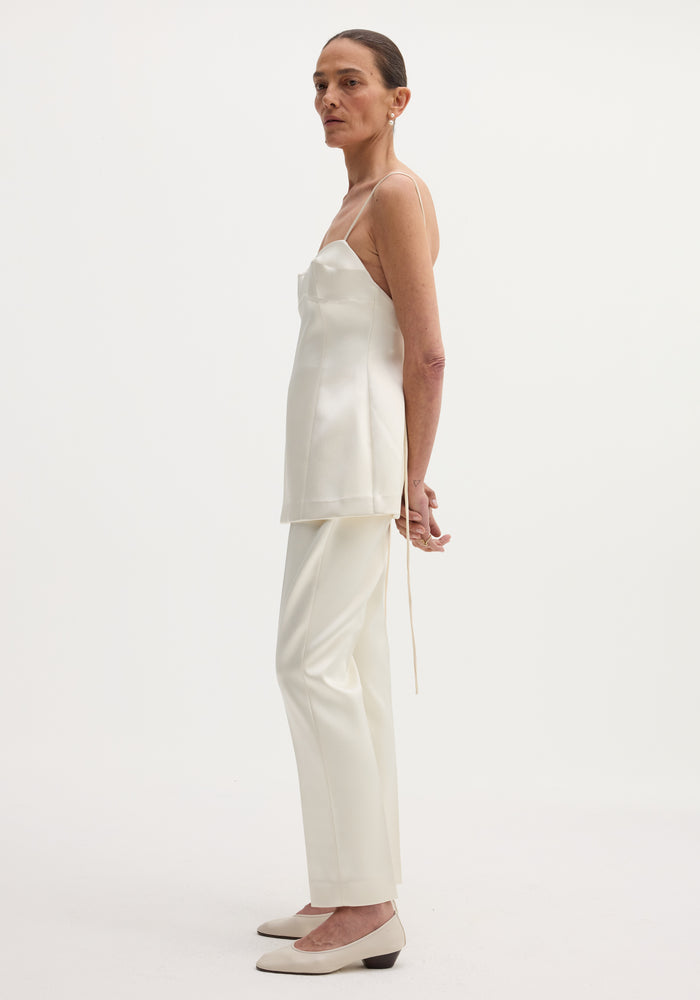 Satin bustier top in ivory showcased on a model with a fitted waist, bustier-style stitching, and adjustable straps, paired with matching straight-leg trousers.