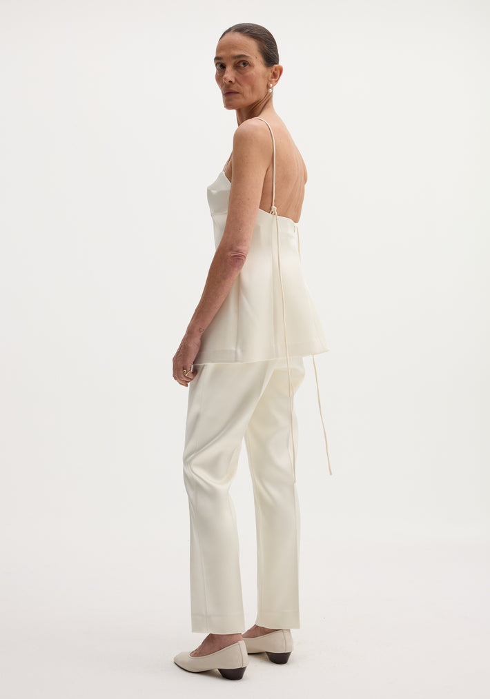 Model wearing Satin bustier top | ivory, showcasing its low-back design, bustier stitching, and long adjustable straps, paired with matching trousers and pointed-toe pumps.