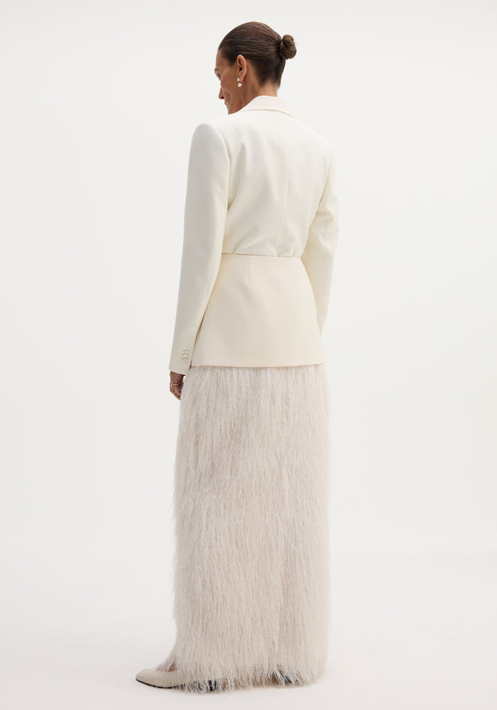 Model in off-white blazer showcasing the Fringe skirt | ivory, featuring a fitted wool upper and full-length fringe, with pointed-toe heels visible.