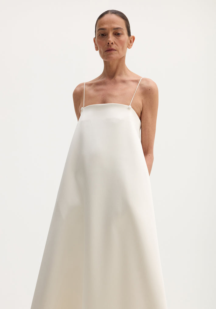 Model in ivory Voluminous satin dress with thin adjustable straps, bandeau bodice, and flared silhouette, button details at strap base visible.