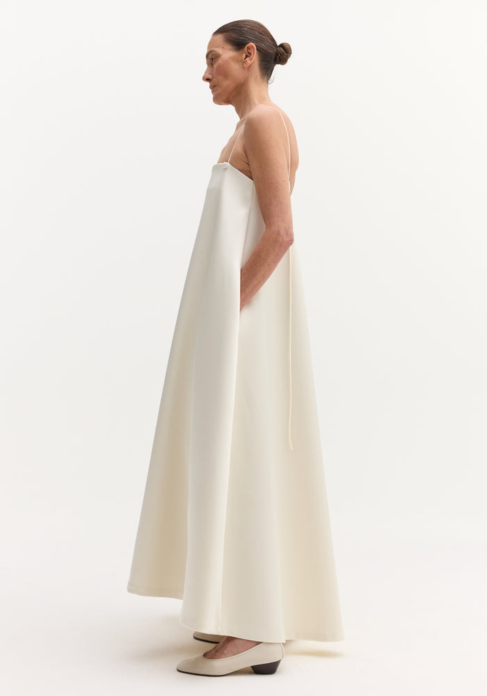 Side profile of a woman in a Voluminous satin dress | ivory with adjustable spaghetti straps, open back, and hidden pockets, styled with a neat bun.