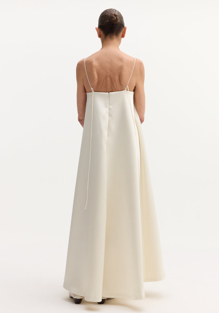 Woman in Voluminous satin dress | ivory, seen from behind, wearing a floor-length gown with adjustable spaghetti straps tying at the back, and button details.
