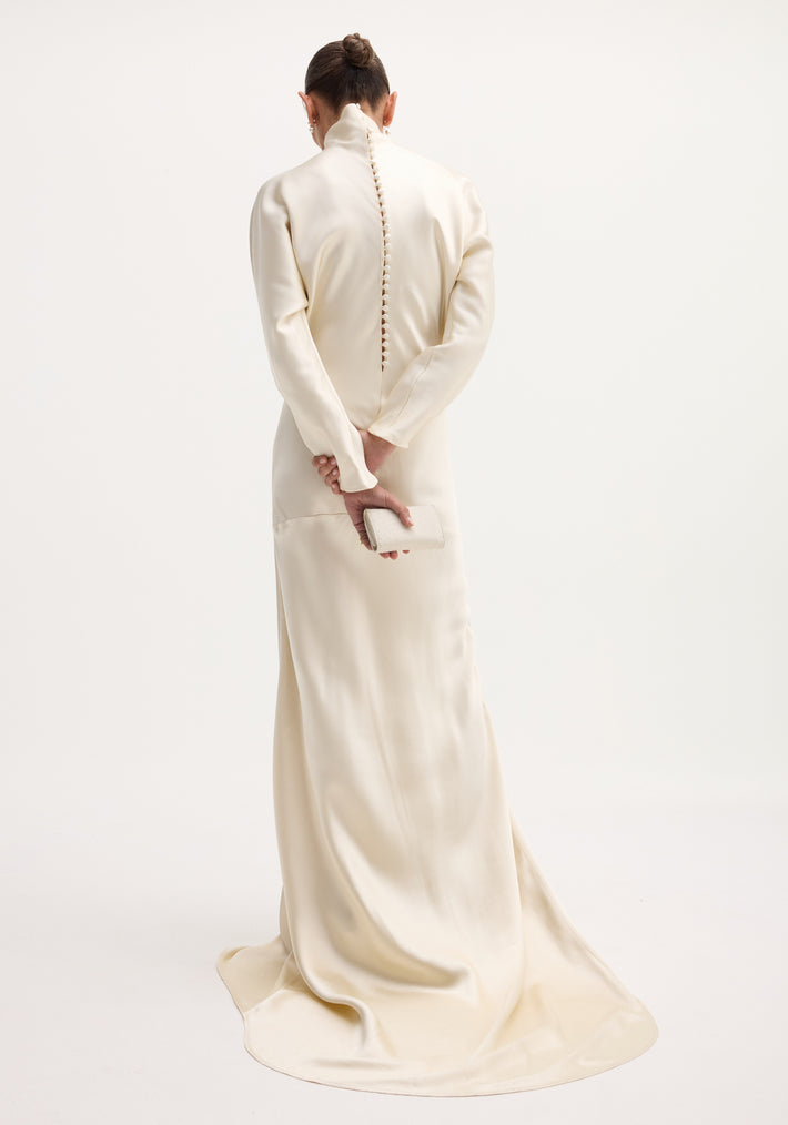 Person in ivory Satin button down dress with train, high collar, long sleeves, covered buttons down back, holding a matching clutch, elegant train pooling on floor.