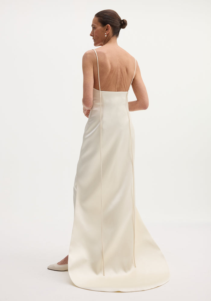 Woman in an ivory satin bustier dress with a train, spaghetti straps, open back, and drop earrings, standing against a white background.