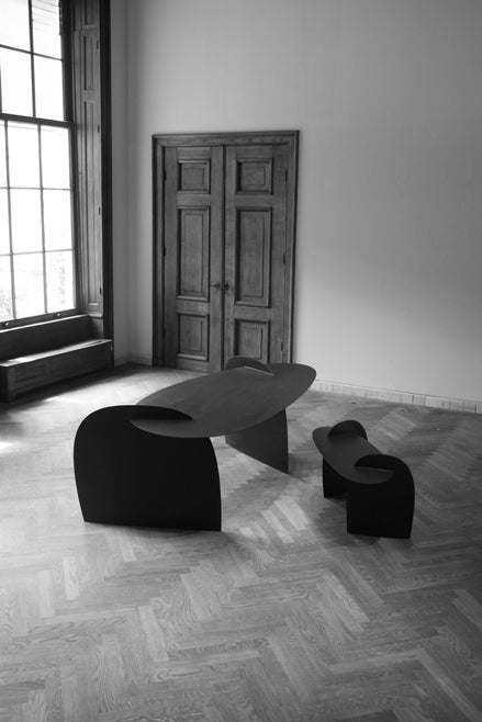 Sculpted Table | 9845: Two matte-black, abstract oak tables by Arne Kristian, showcased in a spacious room with herringbone floors and natural light through a large window.