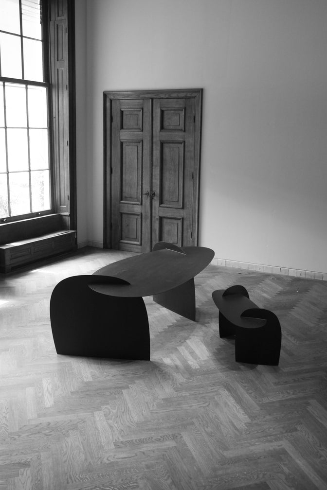 Sculpted Table | 9845: Two matte-black, abstract oak tables by Arne Kristian, showcased in a spacious room with herringbone floors and natural light through a large window.