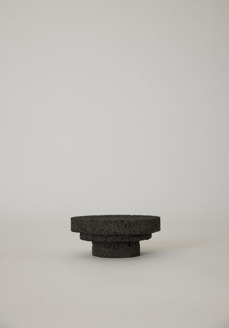 Elevated Sculptural Tray: A handcrafted, three-tiered circular pedestal made from dark lava stone by artist Louis Crombag, showcasing a unique, porous texture.