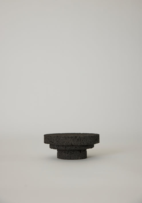 Elevated Sculptural Tray: A handcrafted, three-tiered circular pedestal made from dark lava stone by artist Louis Crombag, showcasing a unique, porous texture.