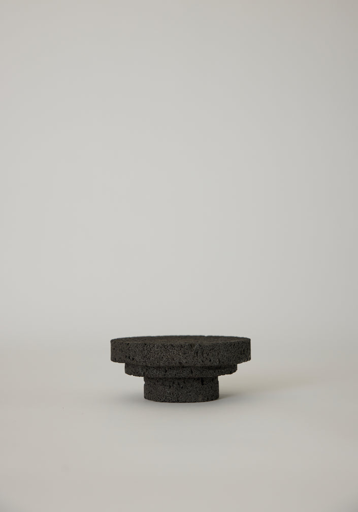 Elevated Sculptural Tray: A handcrafted, three-tiered circular pedestal made from dark lava stone by artist Louis Crombag, showcasing a unique, porous texture.