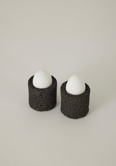 Egg Cups crafted from lava stone, shown in a minimalist setting with a linen napkin and teaspoon, highlighting their unique, handcrafted design.