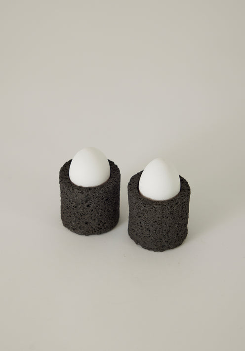 Egg Cups crafted from lava stone, shown in a minimalist setting with a linen napkin and teaspoon, highlighting their unique, handcrafted design.