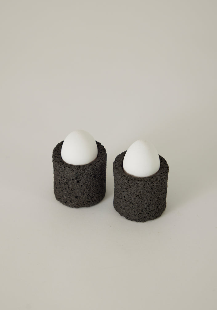 Egg Cups crafted from lava stone, shown in a minimalist setting with a linen napkin and teaspoon, highlighting their unique, handcrafted design.