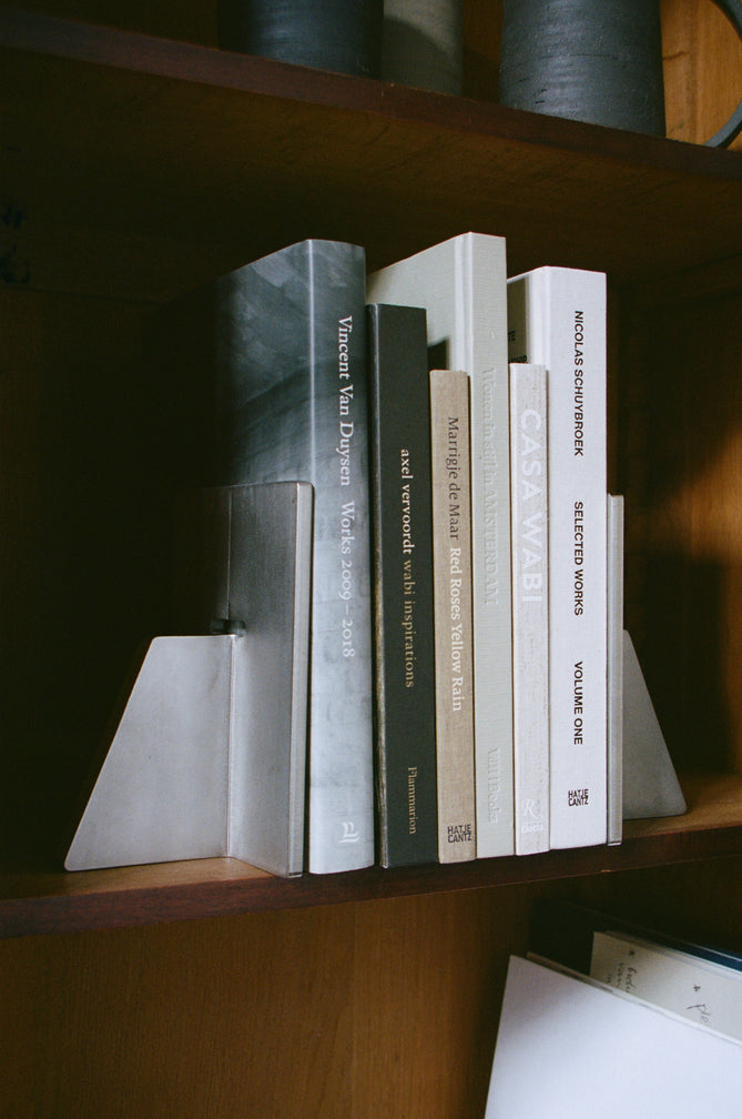 Stainless steel bookends by Paul Coenen hold architecture books upright on a wooden shelf, paired with minimalist design and handcrafted in the Netherlands.