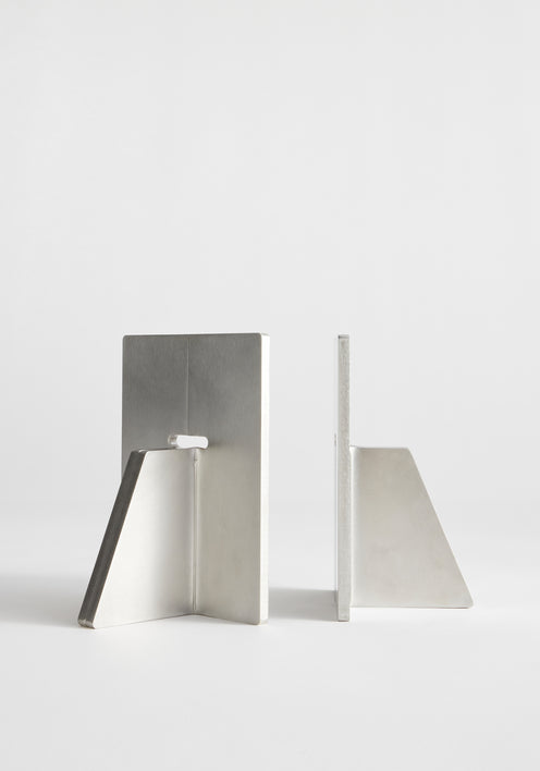 Stainless steel bookends by Paul Coenen hold architecture books upright on a wooden shelf, paired with minimalist design and handcrafted in the Netherlands.
