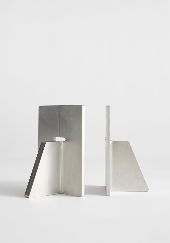 Stainless steel bookends by Paul Coenen hold architecture books upright on a wooden shelf, paired with minimalist design and handcrafted in the Netherlands.
