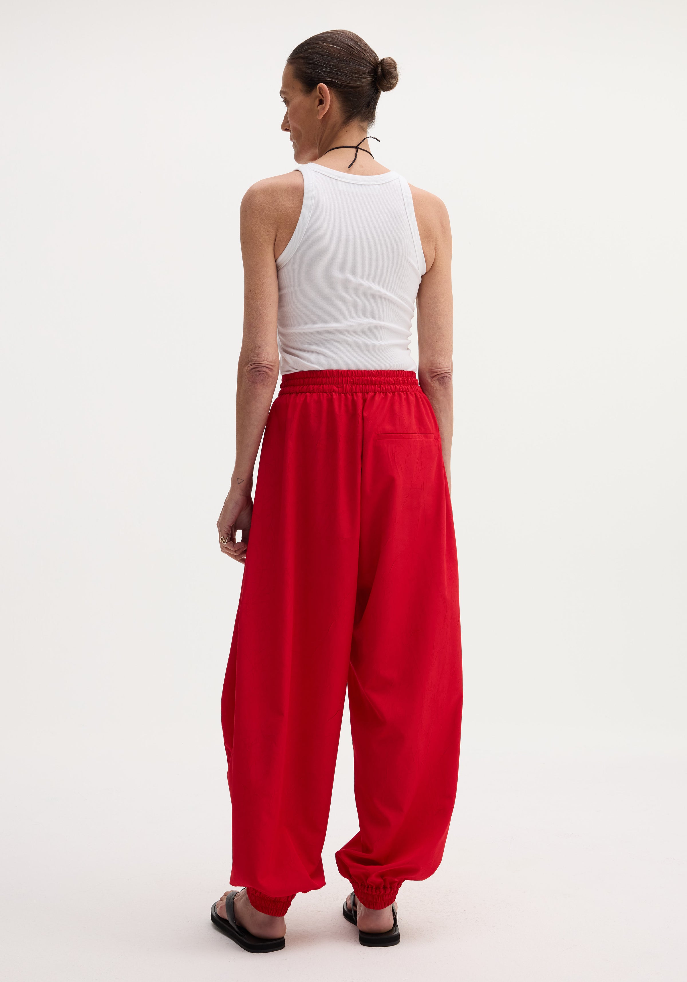 Back view of person in Balloon track pants with elastic cuffs, wearing a white tank top and black slide sandals, showcasing the pants' voluminous design.