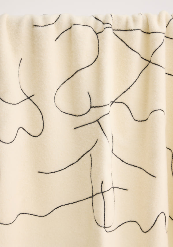 Tulip embroidered mohair blanket in off white, featuring an abstract black line pattern. Crafted from Italian-made brushed wool, showcasing chunky fringes and a soft, textured finish.