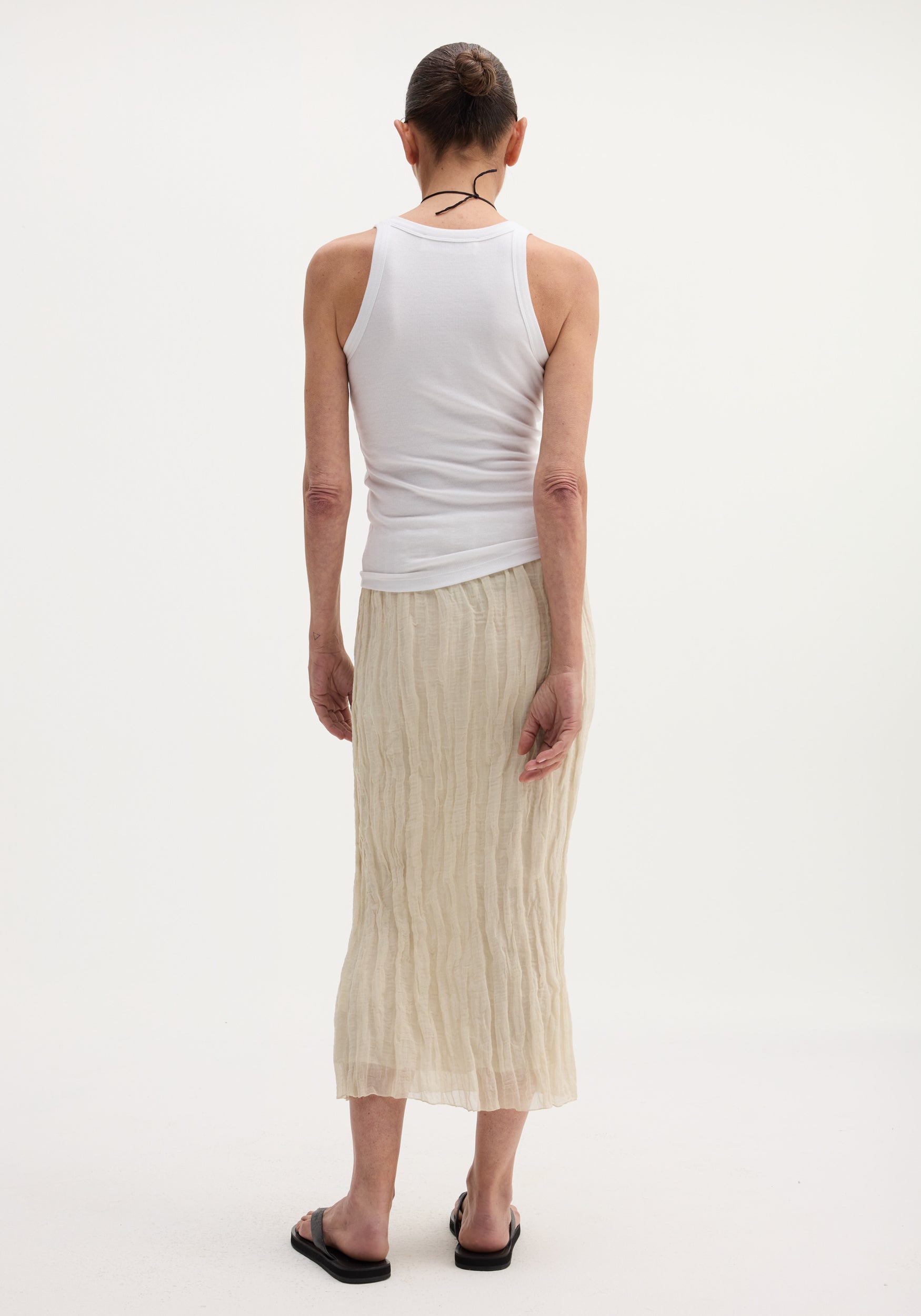 Person wearing a Textured tube skirt | cream, featuring a crinkled, mid-calf length with an elastic waistband, paired with a white tank top and black sandals.