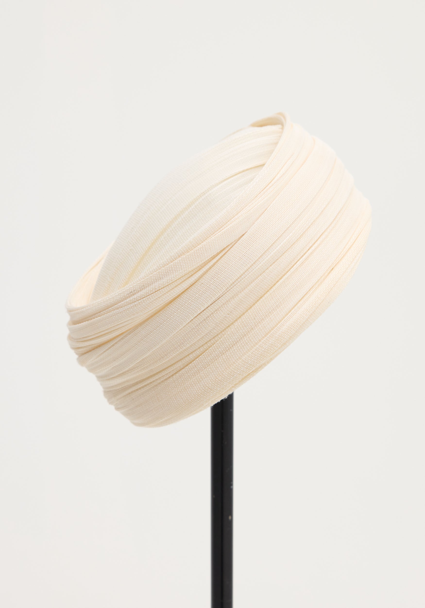 Sculptural silk hat in ivory, elegantly draped with finely pleated silk tulle, crafted by a Dutch artist, displayed on a slender black stand.