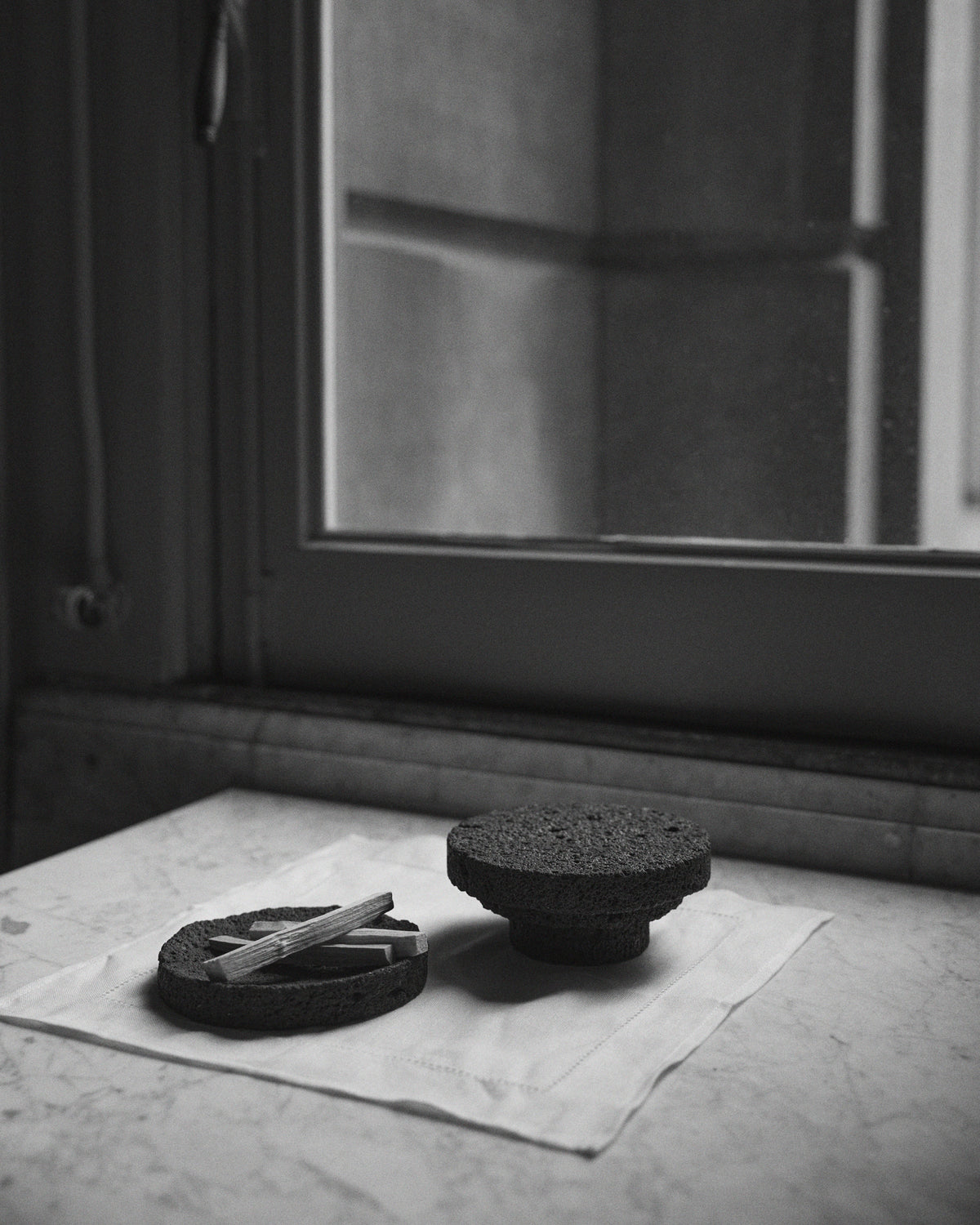 Elevated Sculptural Tray: a handcrafted lava stone tray on a pedestal, featuring a minimalist design with a porous texture, displayed on a cloth-covered stone ledge.