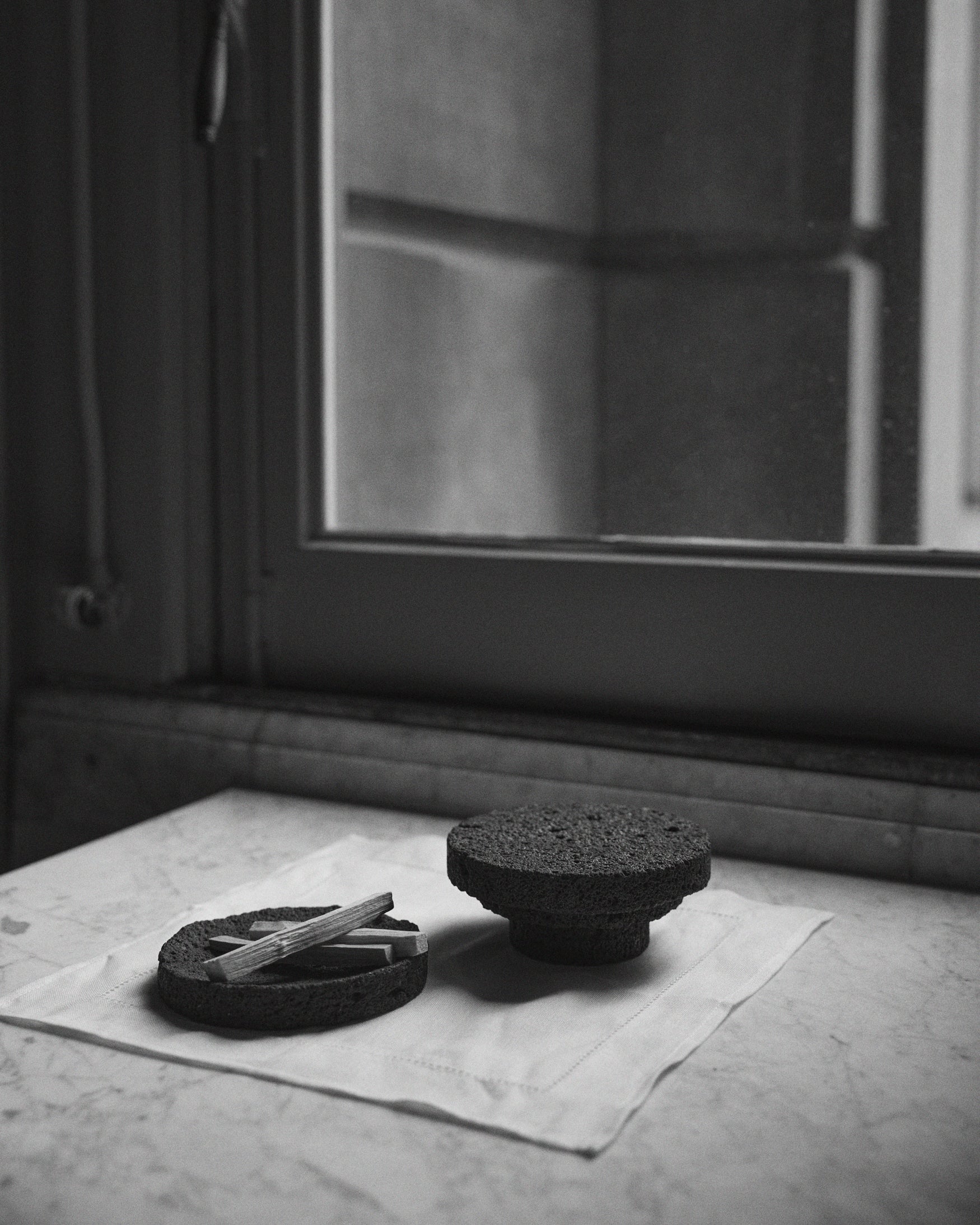 Elevated Sculptural Tray: a handcrafted lava stone tray on a pedestal, featuring a minimalist design with a porous texture, displayed on a cloth-covered stone ledge.