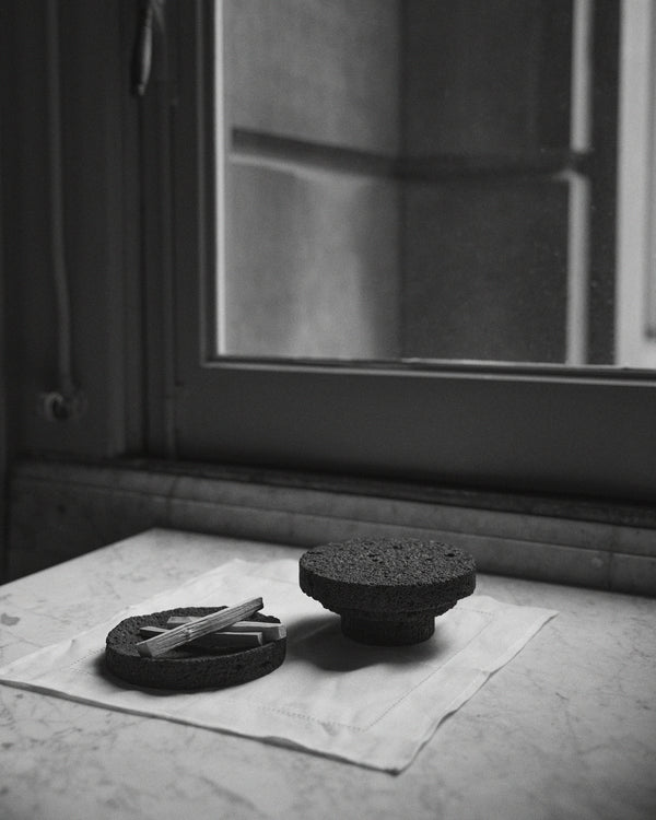Elevated Sculptural Tray: a handcrafted lava stone tray on a pedestal, featuring a minimalist design with a porous texture, displayed on a cloth-covered stone ledge.