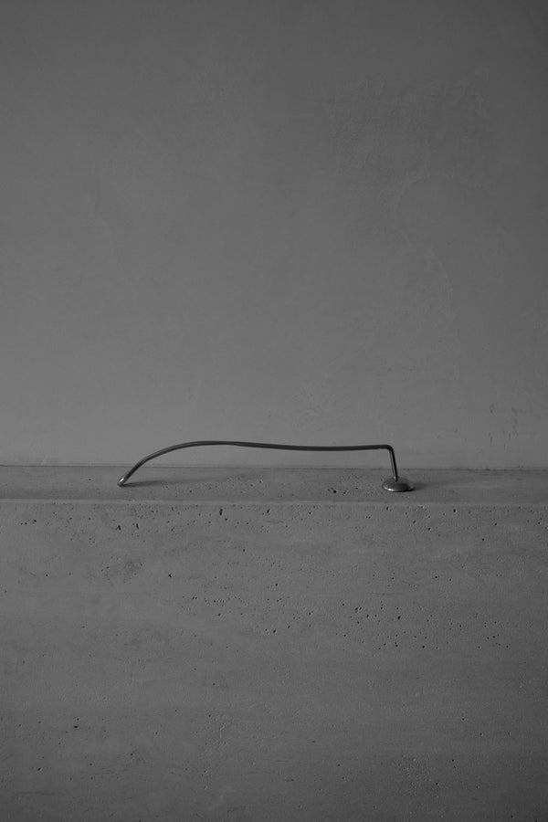 Candle Stopper | silver depicted as a sleek, upward-spiraling stainless steel rod elegantly bridging a smooth concrete ledge and wall, embodying minimalist architectural design.