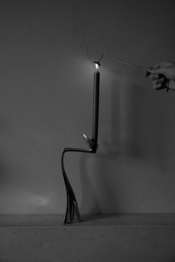 Candle Stopper | silver shown with a taper candle in a sculptural metal holder, a hand using a snuffer to extinguish the flame. Monochrome emphasizes the elegant design.