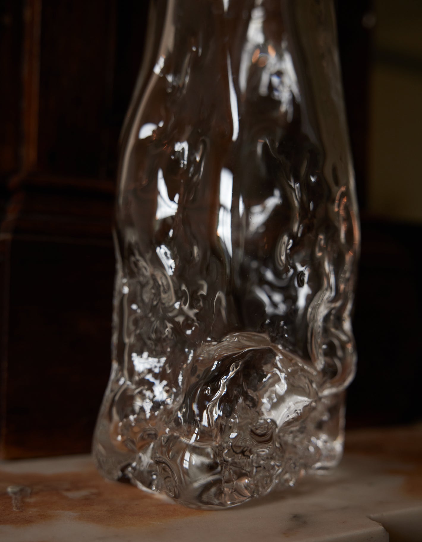 Blown vase | Glass: A clear, abstract glass sculpture with wavy distortions, hand-blown for uniqueness, sits on a stone surface, emphasizing organic, molten beauty.