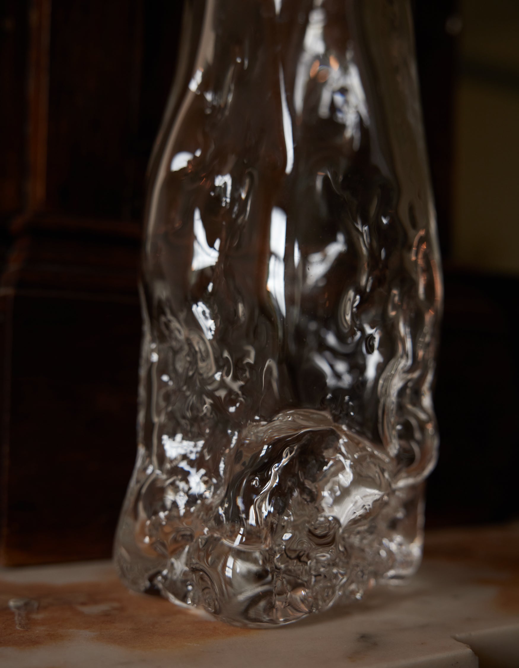 Blown vase | Glass: A clear, abstract glass sculpture with wavy distortions, hand-blown for uniqueness, sits on a stone surface, emphasizing organic, molten beauty.