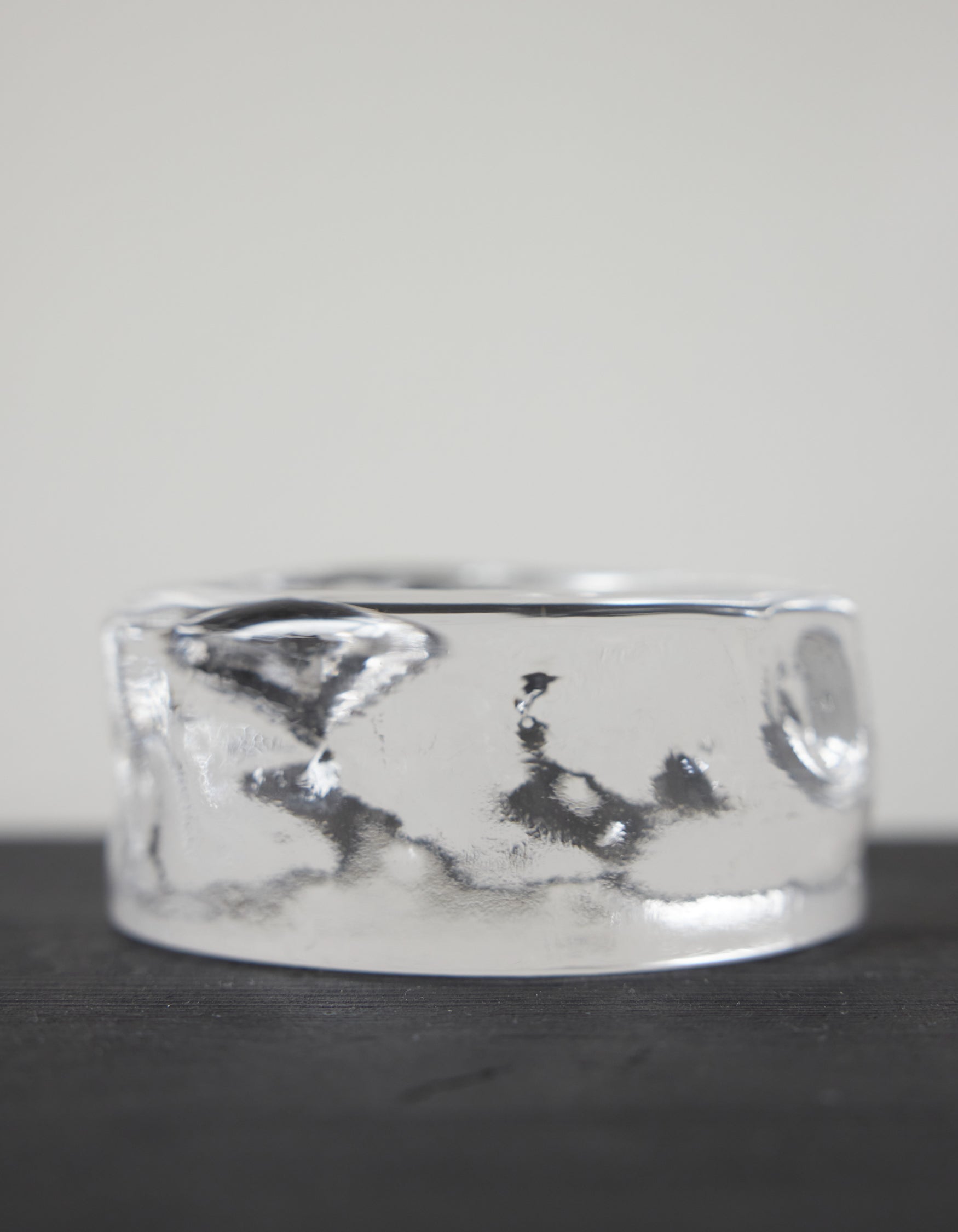 Presse-papier & holder by Szkło Studio: A clear, cylindrical glass ring, showcasing unique hand-blown craftsmanship, resting on a dark surface.
