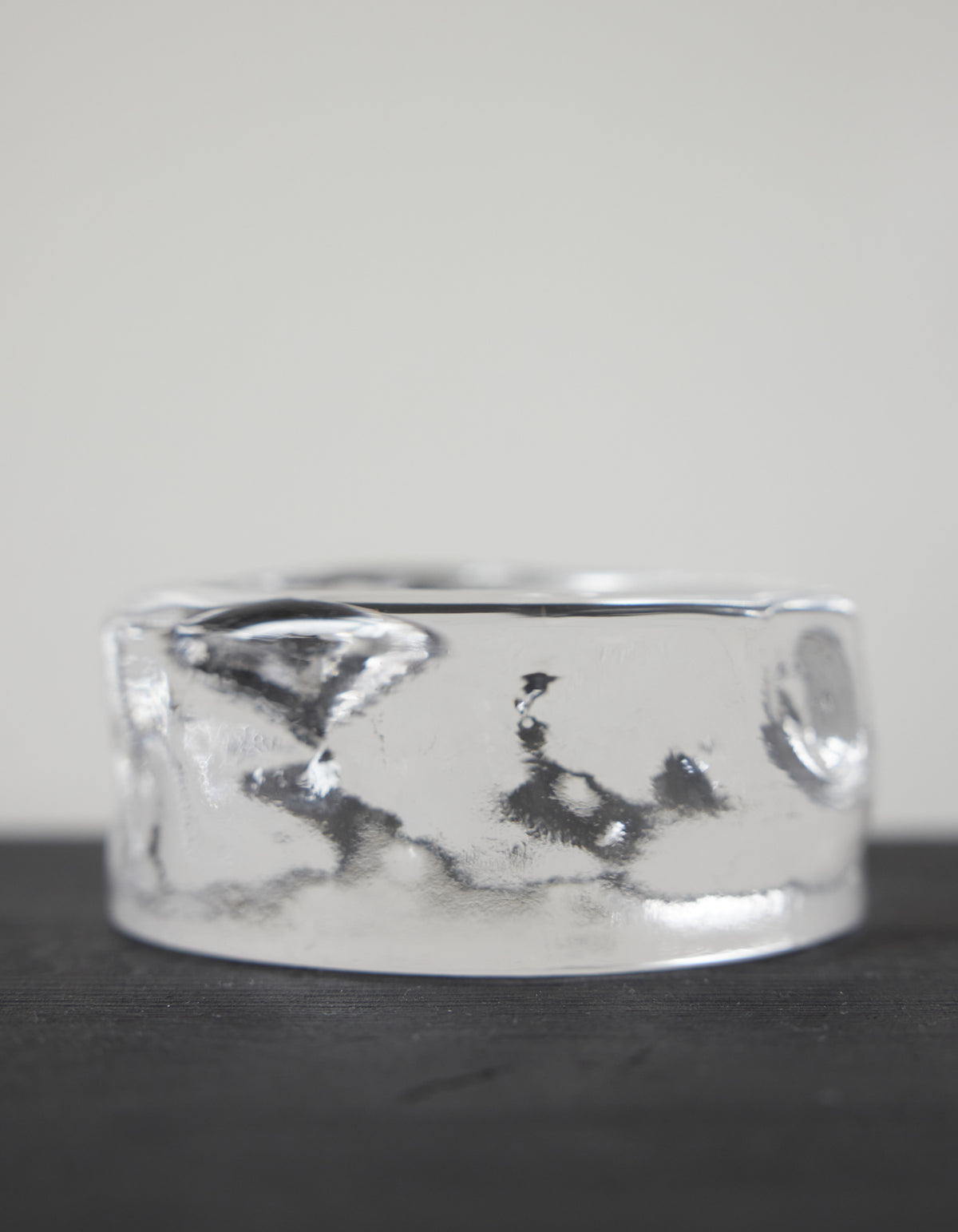 Presse-papier & holder by Szkło Studio: A clear, cylindrical glass ring, showcasing unique hand-blown craftsmanship, resting on a dark surface.