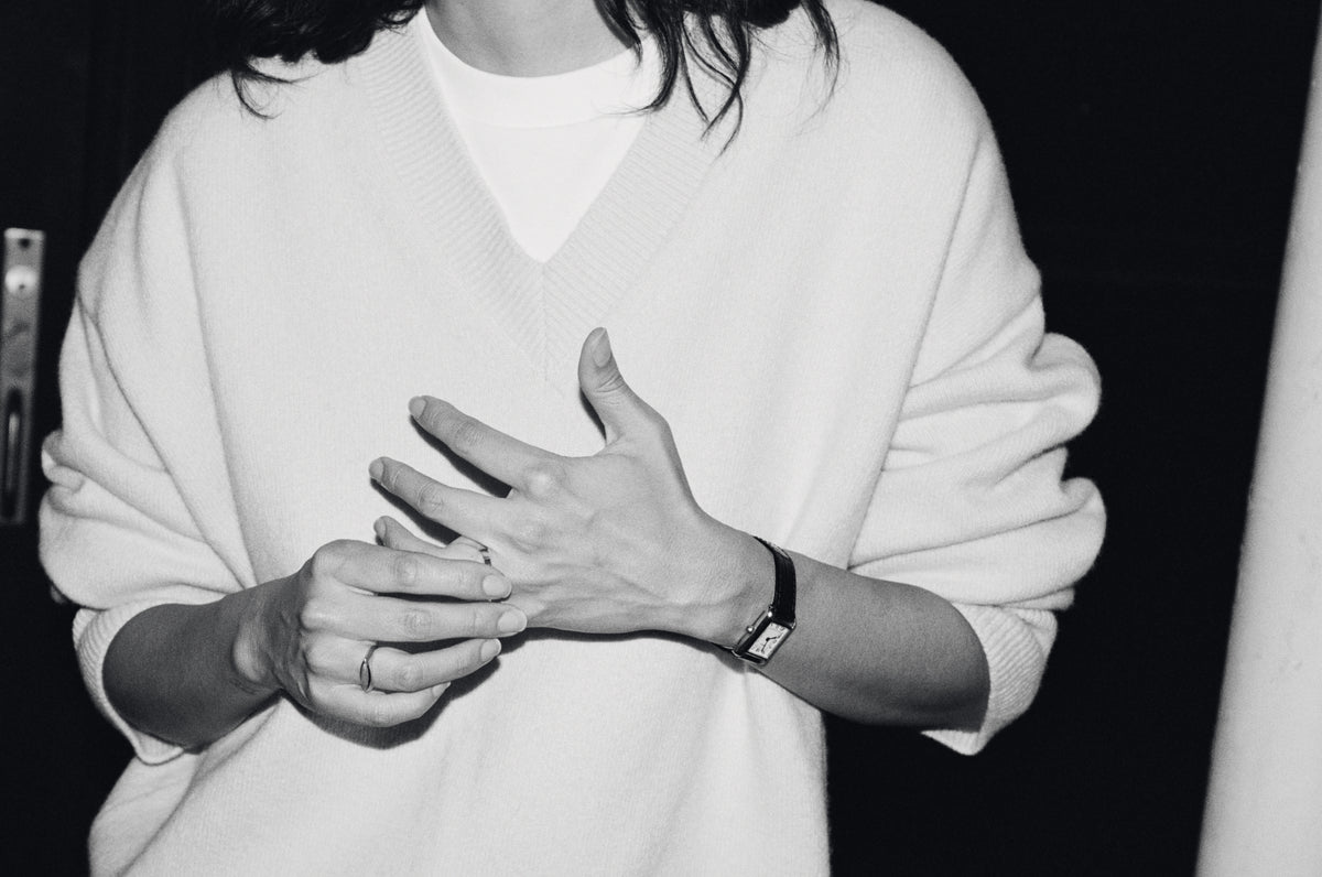 Black and white photo of a person in a white sweater holding their hands together and wearing a wristwatch and rings