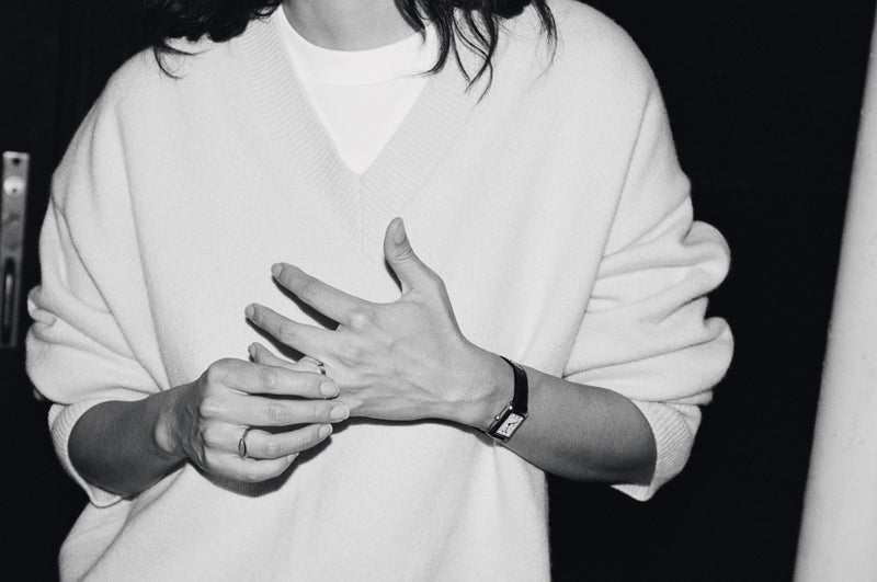 Black and white photo of a person in a white sweater holding their hands together and wearing a wristwatch and rings