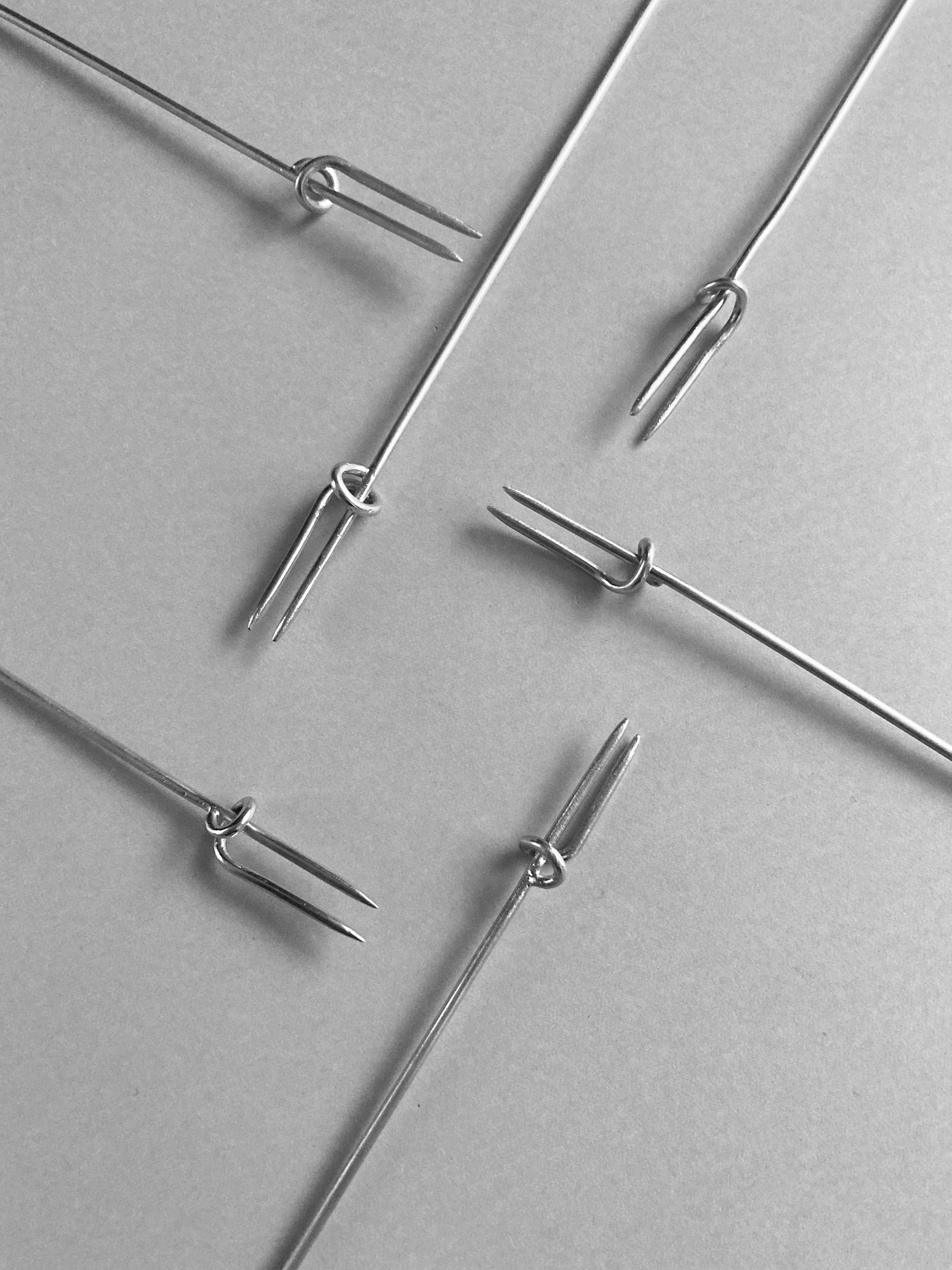 Close-up of multiple thin metal tools with two-pronged ends arranged on a flat surface, each called a Vine Fork, used for delicate work or handling small items.