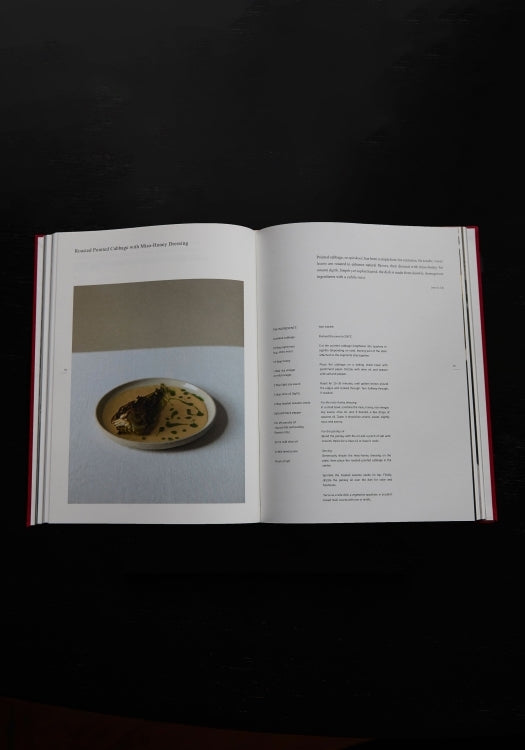 Róhe Cookbook | red, open to a page with a plated dish photo and accompanying recipe, featuring reimagined Dutch cuisine from Huis de Vicq's creative kitchen.
