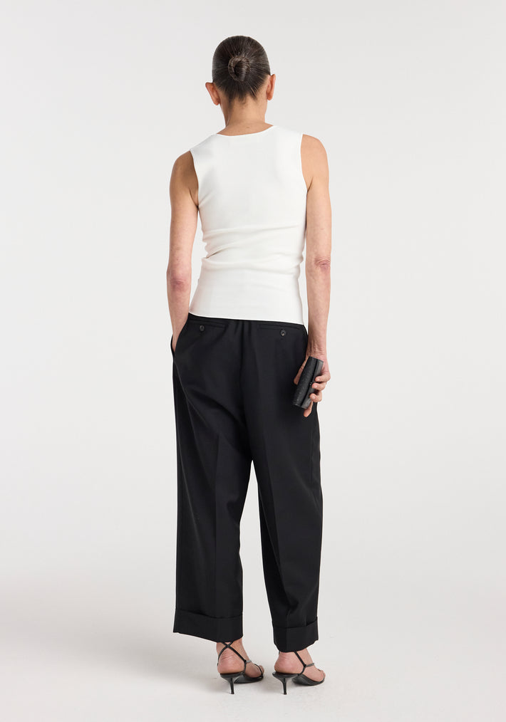 Woman seen from the back wearing a Bustier shaped knitted top | optic white, paired with black wide-leg trousers and black heeled sandals, holding a small black clutch purse.