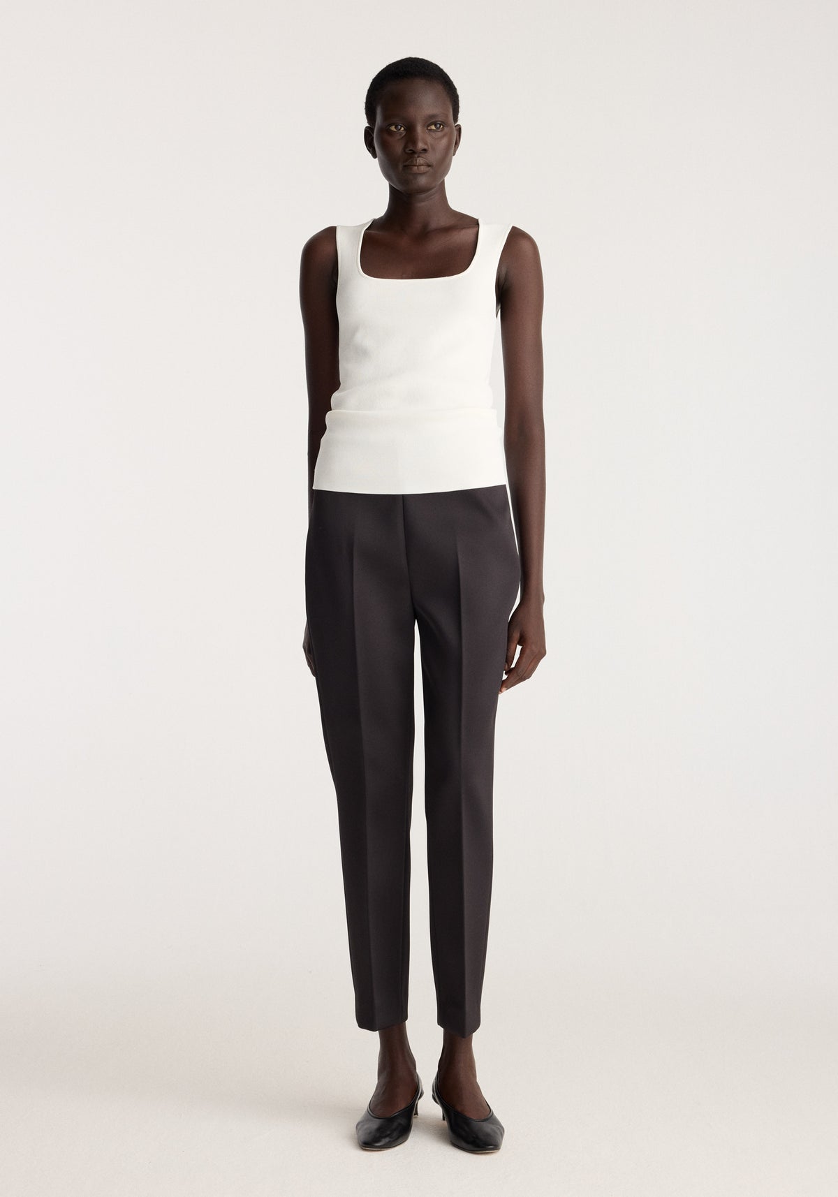 Bustier shaped knitted top | optic white shown on a model with a fitted sleeveless silhouette and square neckline styled with dark tailored trousers