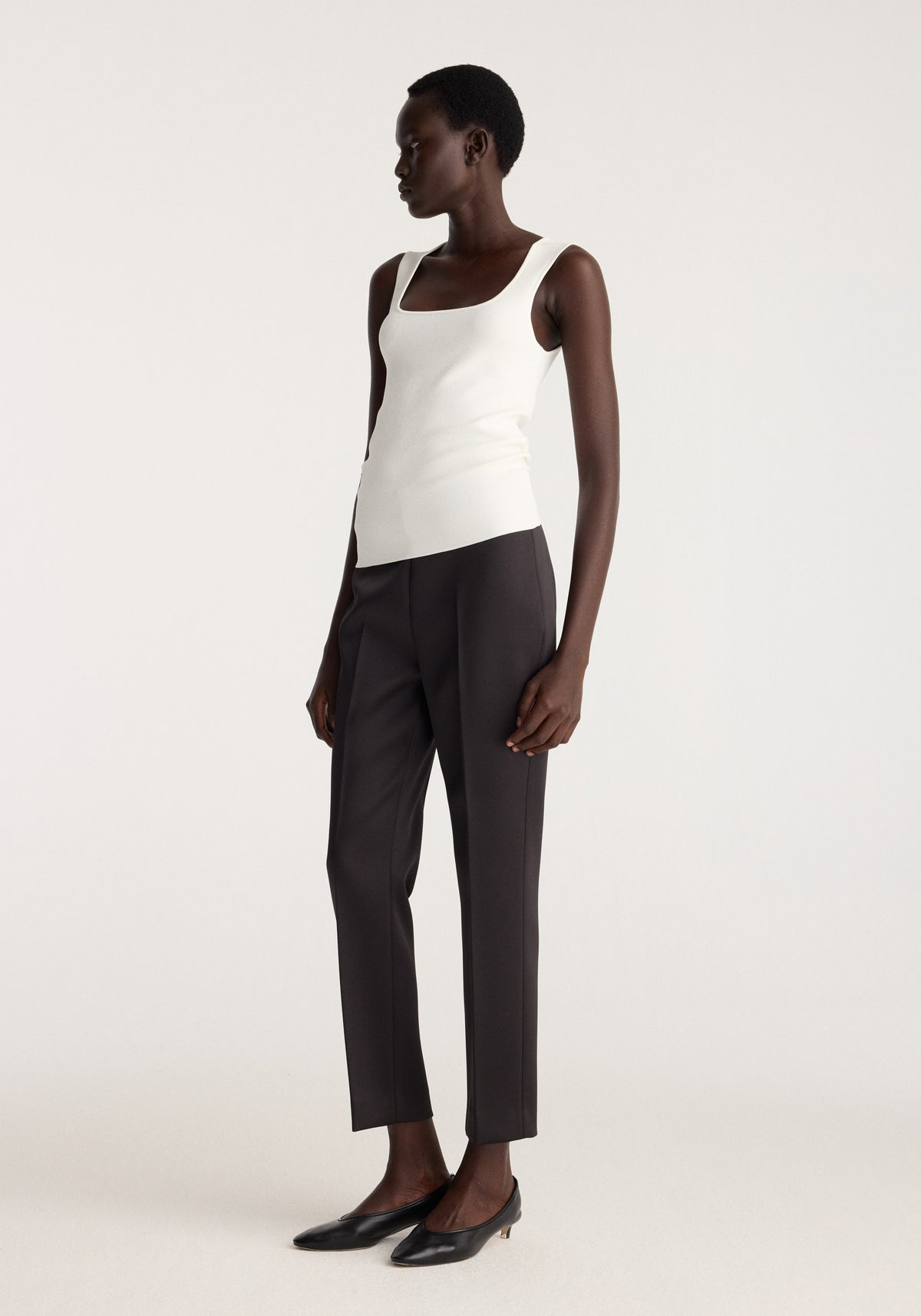 Bustier shaped knitted top | optic white worn by a model with dark tailored trousers and black pointed shoes against a neutral studio background